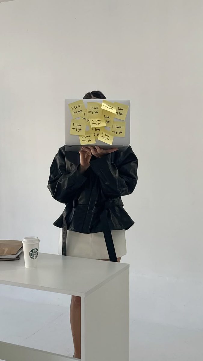 A person holding a laptop covered in “I love my job” sticky notes over their face